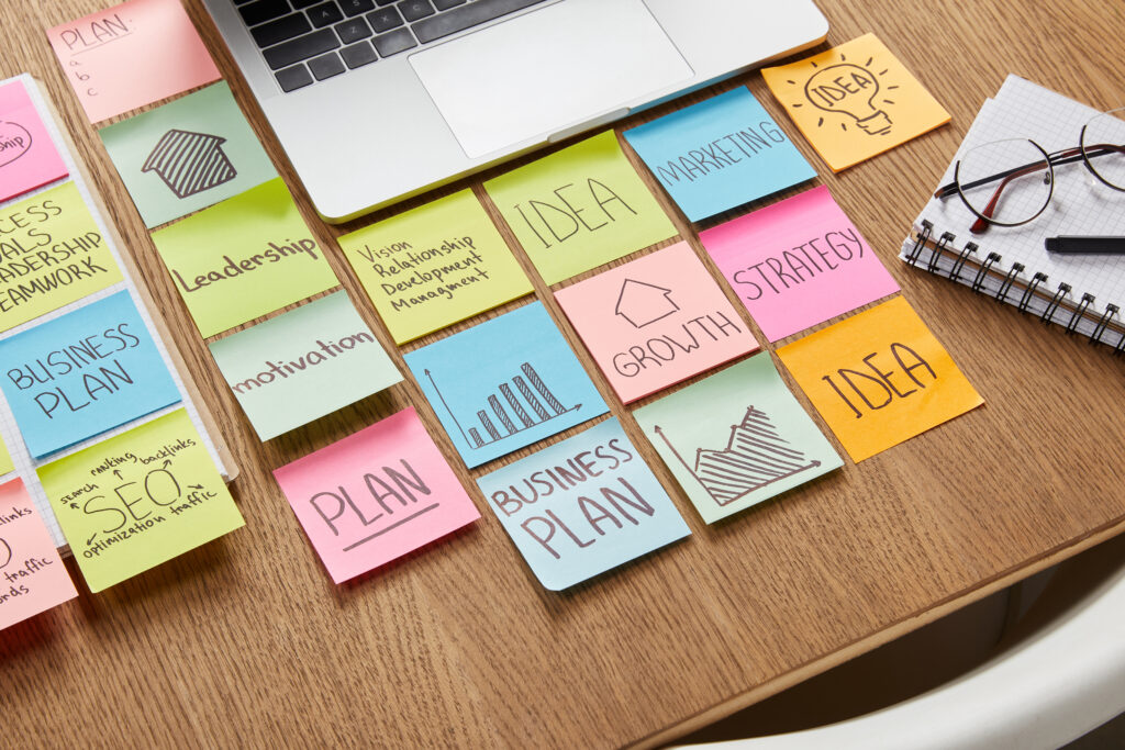 desk with laptop and sticky notes with random business words and sketches